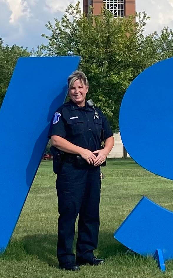 Betsy Wessels standing in front of the GVSU sign wearing her old police officer uniform.